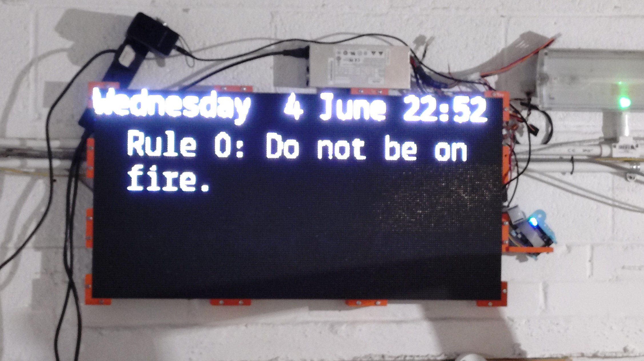 The LED Display reading "Wednesday 4 June 22:52 Rule 0: Do not be on fire", it is mounted somewhat untidily on a wall